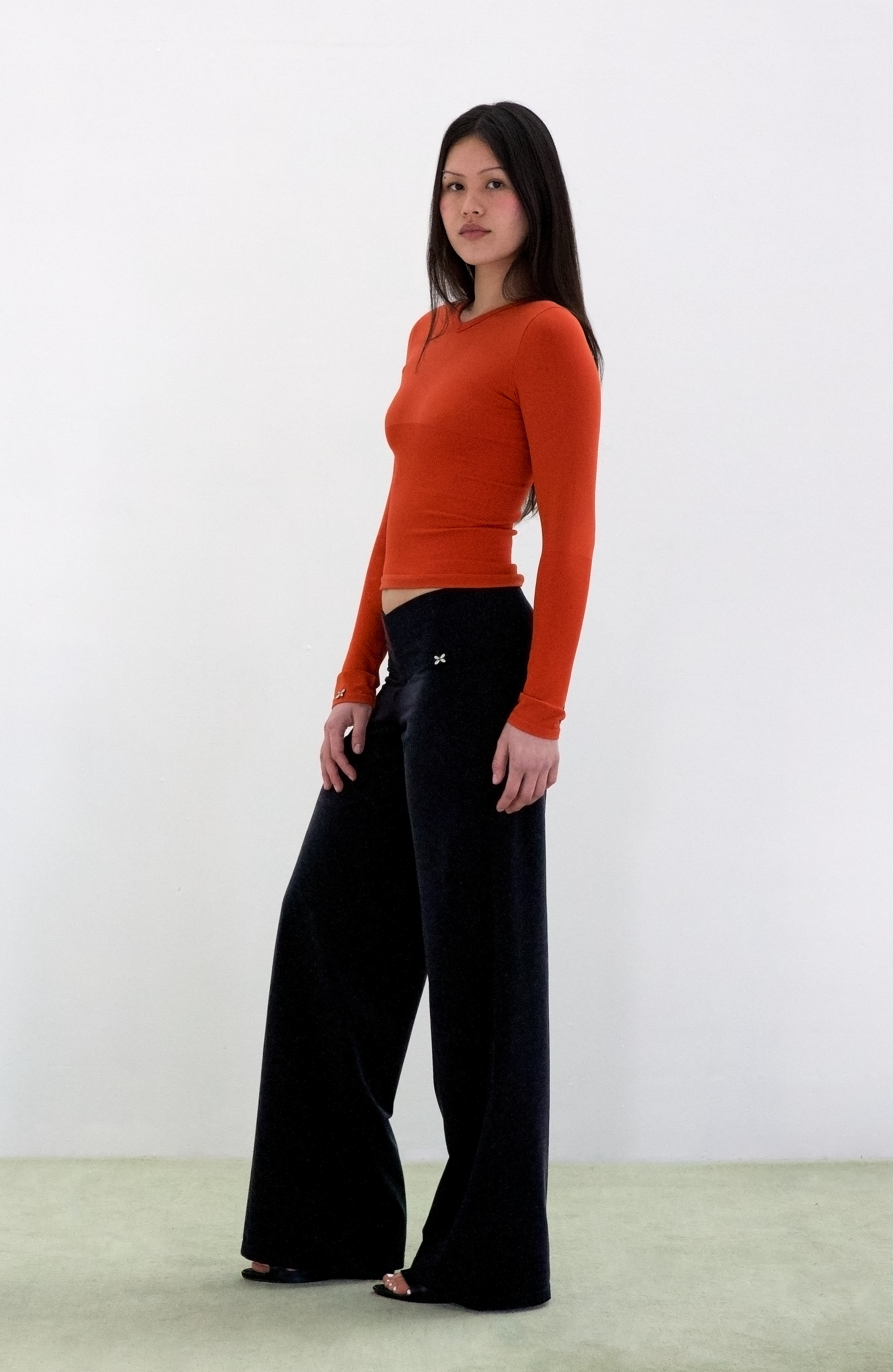Woman wearing an orange long-sleeve top and black pants on a white background