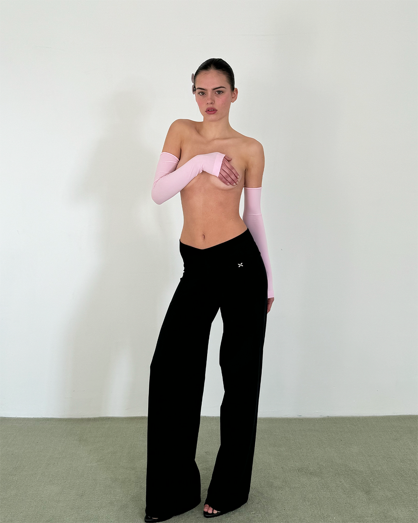 Woman wearing black pants and pink arm sleeves against a white background