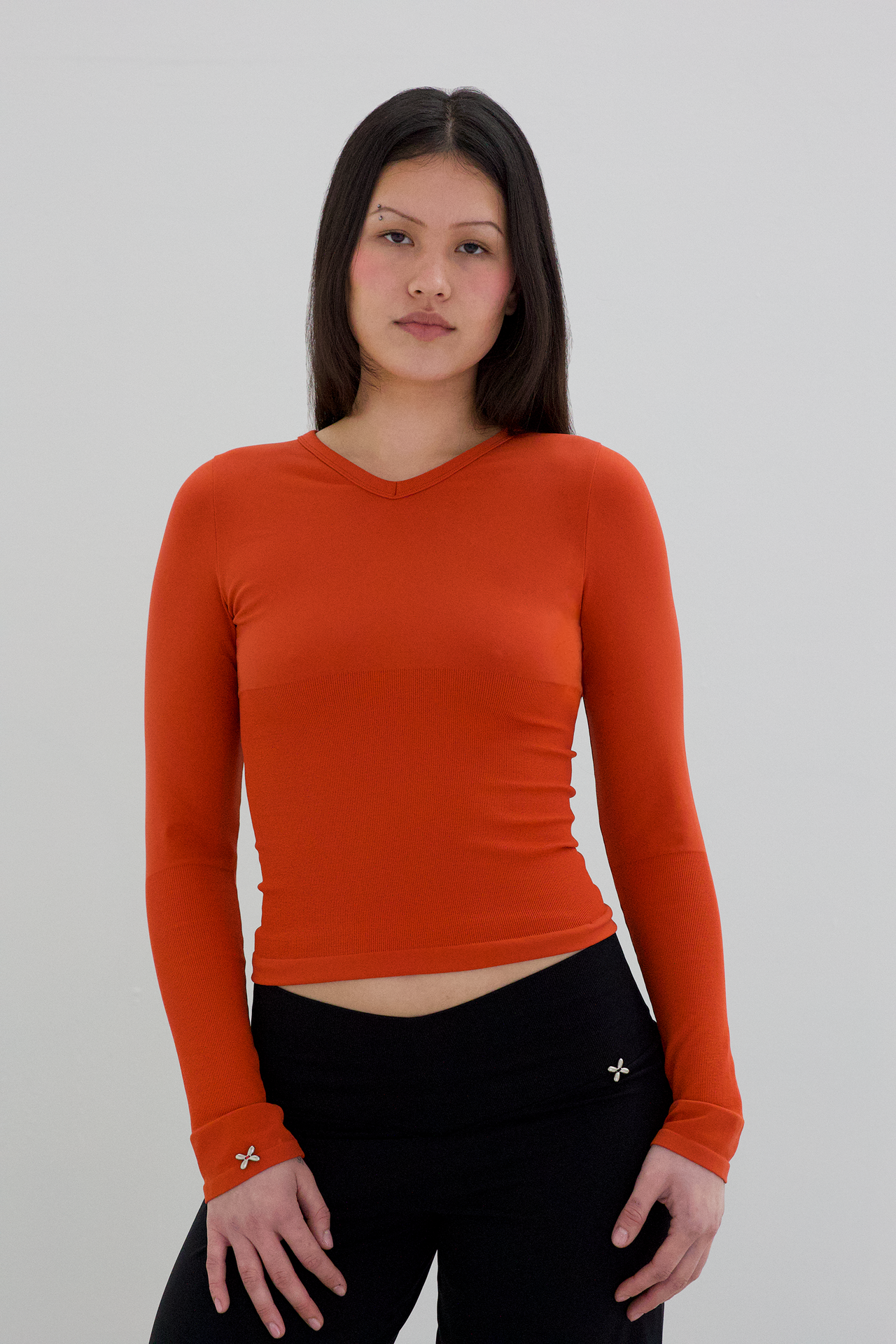 Woman wearing an orange long-sleeve top against a plain background