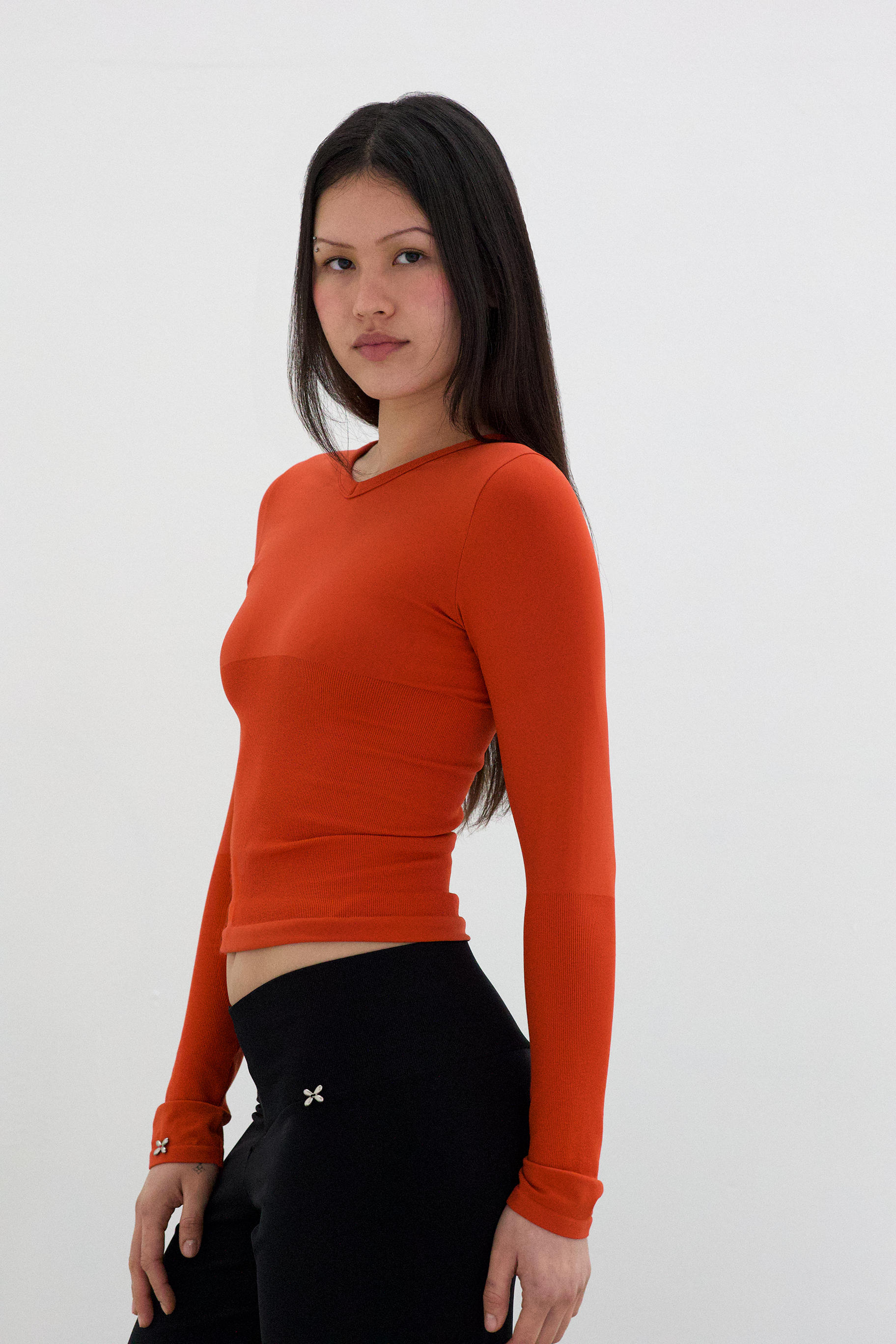 Woman wearing an orange long-sleeve top against a white background