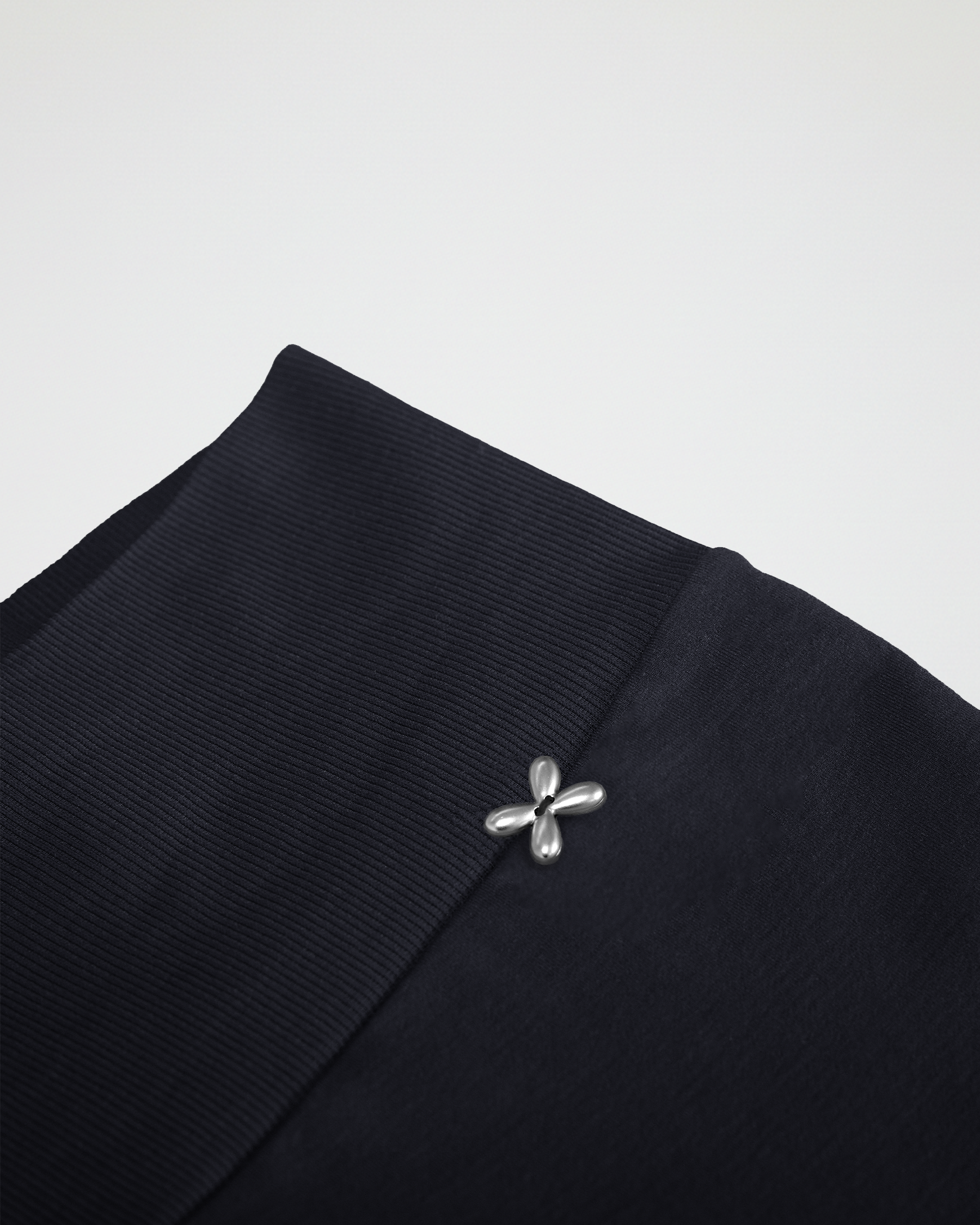 Close-up of a black garment with a silver brooch on a light gray background