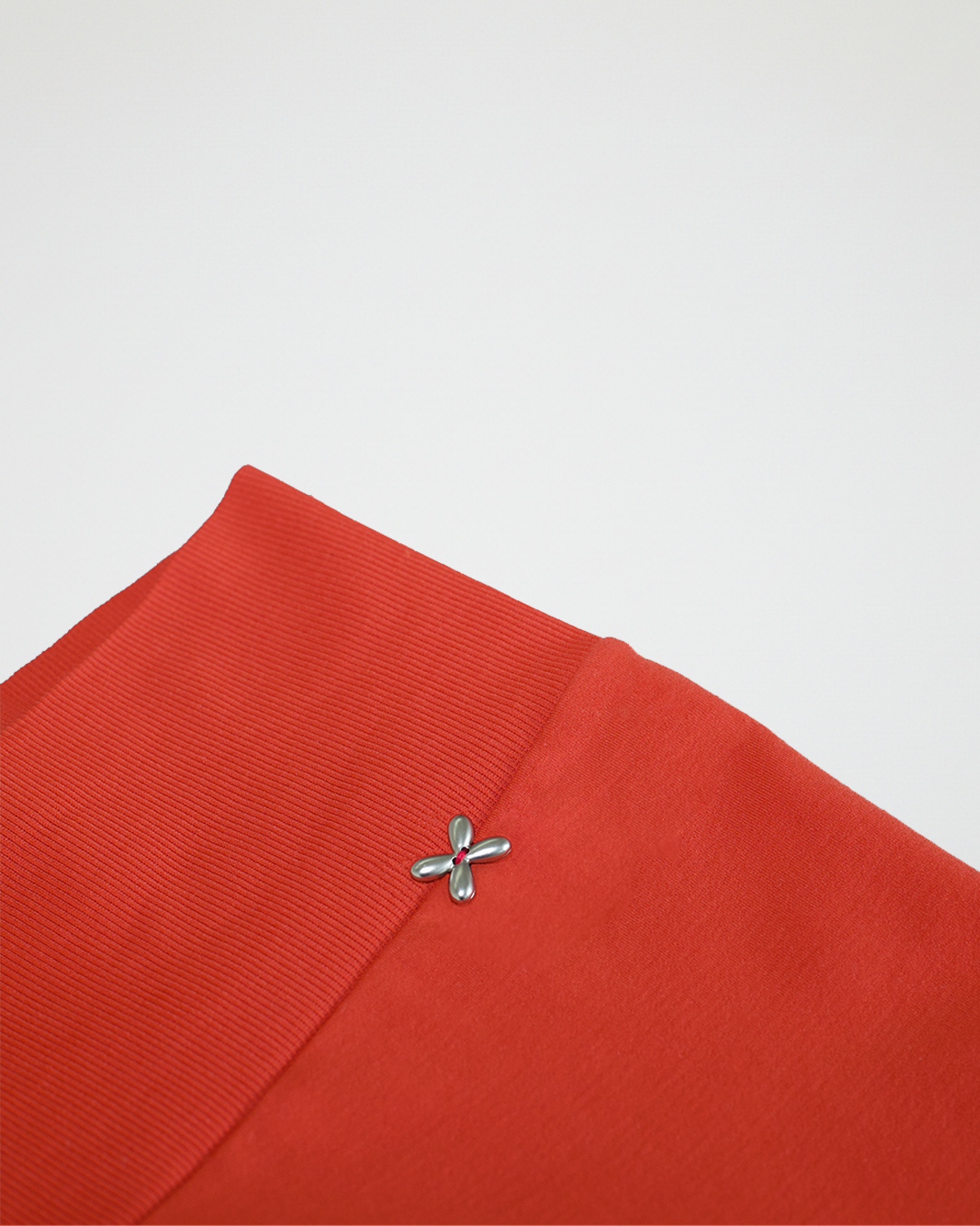 Close-up of a orange fabric with a silver brooch on a light gray background